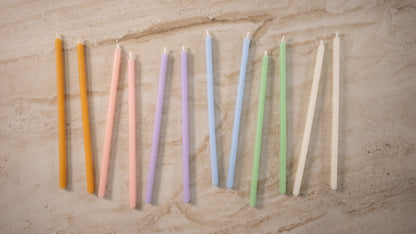Pastel beeswax birthday candles in assorted shades arranged on a neutral stone background — luxury manifesting candle set by The Manifesting Studio.